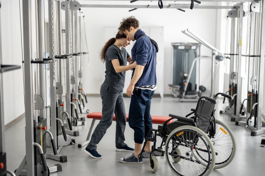Rehabilitation specialist helps a guy stand out of a wheelchair